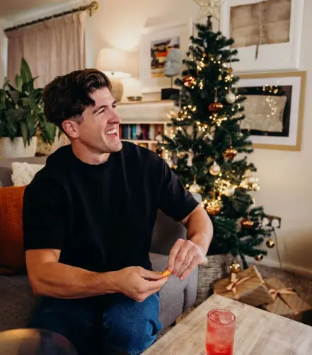 Smiling Danny Campbell sitting on a couch holding his North Star serve, with a notebook on his lap