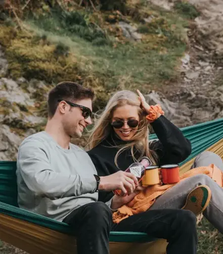 Rona McMillan and her brother sitting side by side in a hammock, pouring Ben Lomond Gin into mugs.