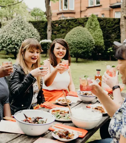 Julie Lin smiling with friends at a picnic, passing food and enjoying her Vivid Horizon Punch in collaboration with Ben Lomond Gin.
